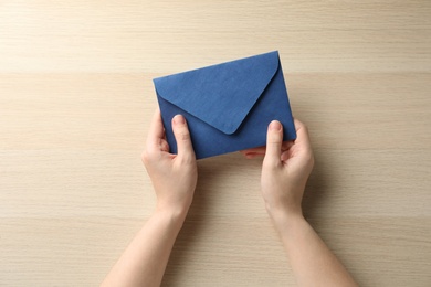 Photo of Woman with blue paper envelope at wooden table, top view