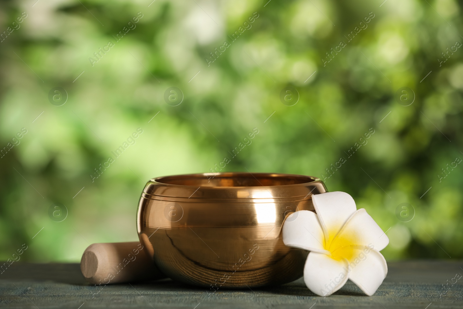 Photo of Golden singing bowl, mallet and flower on blue wooden table outdoors, space for text