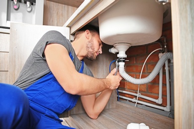 Professional plumber in uniform fixing sink indoors