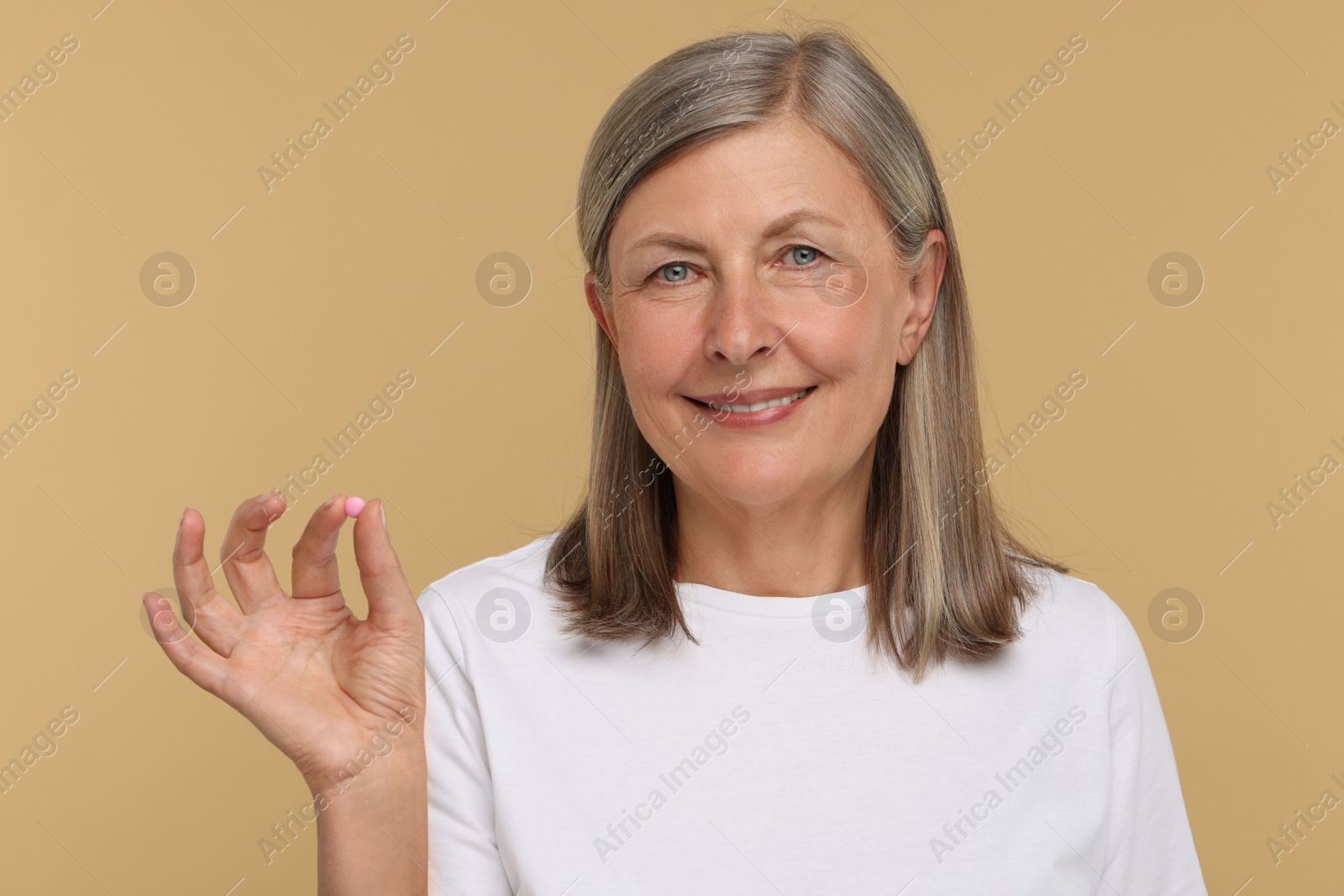 Photo of Senior woman with pill on beige background