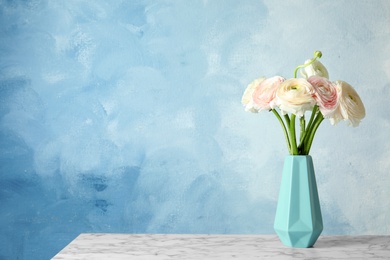 Vase with beautiful ranunculus flowers on table against color background, space for text