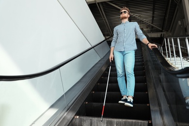 Photo of Blind person with long cane on escalator indoors. Space for text