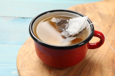 Photo of Tea bag in cup with hot drink on light blue wooden table, closeup