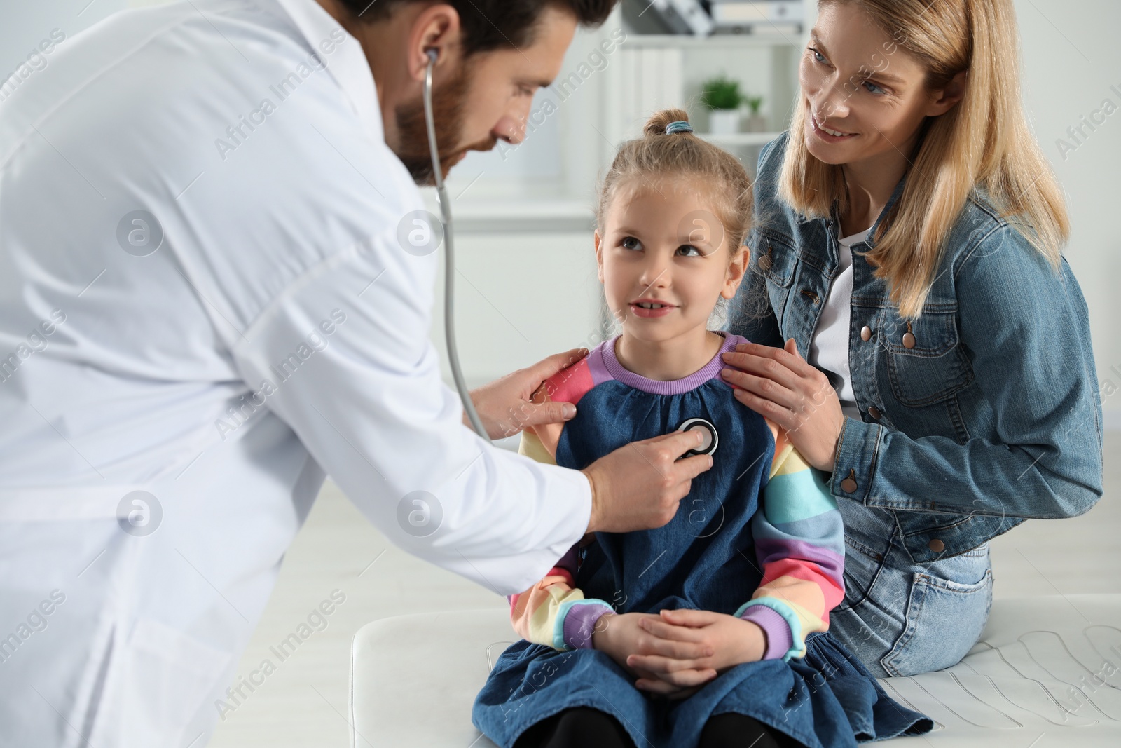 Photo of Mother and daughter having appointment with doctor. Pediatrician examining patient with stethoscope in clinic