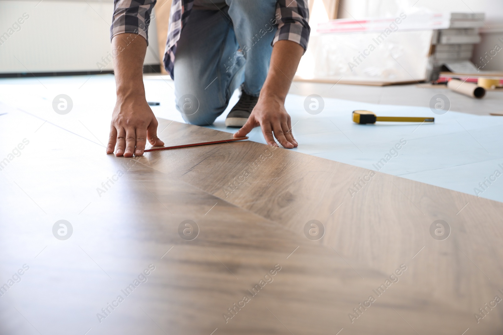 Photo of Worker installing laminated wooden floor indoors, closeup