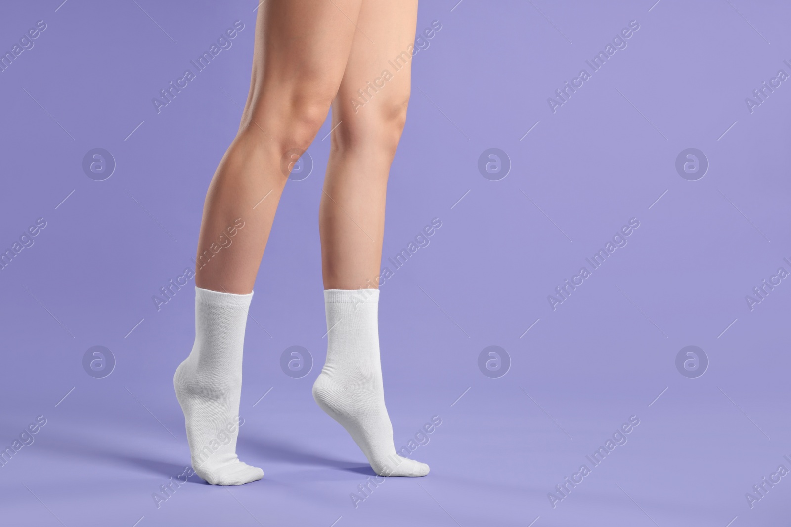 Photo of Woman in stylish white socks on violet background, closeup. Space for text