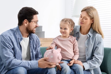 Photo of Planning budget together. Little girl with her parents putting coin into piggybank at home