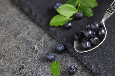 Spoon with tasty fresh bilberries on dark grey table, closeup. Space for text