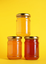 Jars with different types of organic honey on yellow background