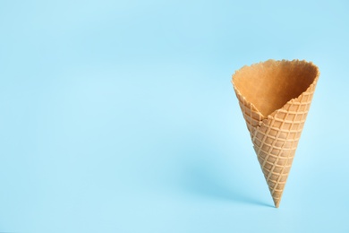 Photo of Empty wafer ice cream cone on blue background. Space for text