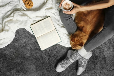 Photo of Woman with cute red cat and book on grey carpet, top view