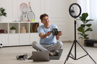 Photo of Smiling sports blogger holding ab roller while streaming online fitness lesson with smartphone at home