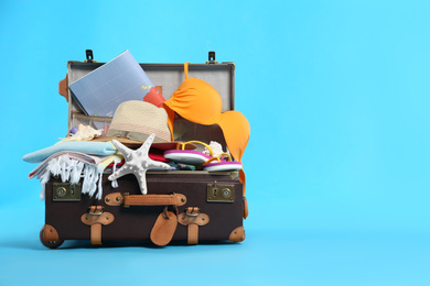 Photo of Packed vintage suitcase with different beach objects on light blue background, space for text. Summer vacation