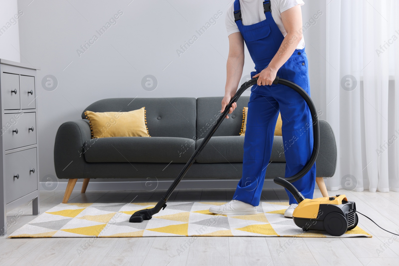 Photo of Dry cleaner's employee hoovering carpet with vacuum cleaner in room, closeup