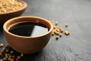 Tasty soy sauce in bowl and soybeans on black table, closeup. Space for text