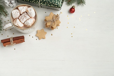 Flat lay composition with delicious marshmallow cocoa and Christmas decor on white wooden table. Space for text