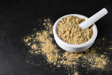 Photo of Mortar with mustard powder on black table. Space for text