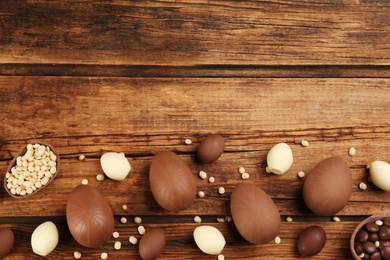 Sweet chocolate eggs and candies on wooden table, flat lay. Space for text