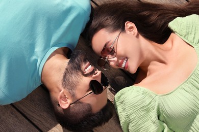 Photo of Beautiful smiling woman and handsome man in sunglasses on wooden deck outdoors, above view