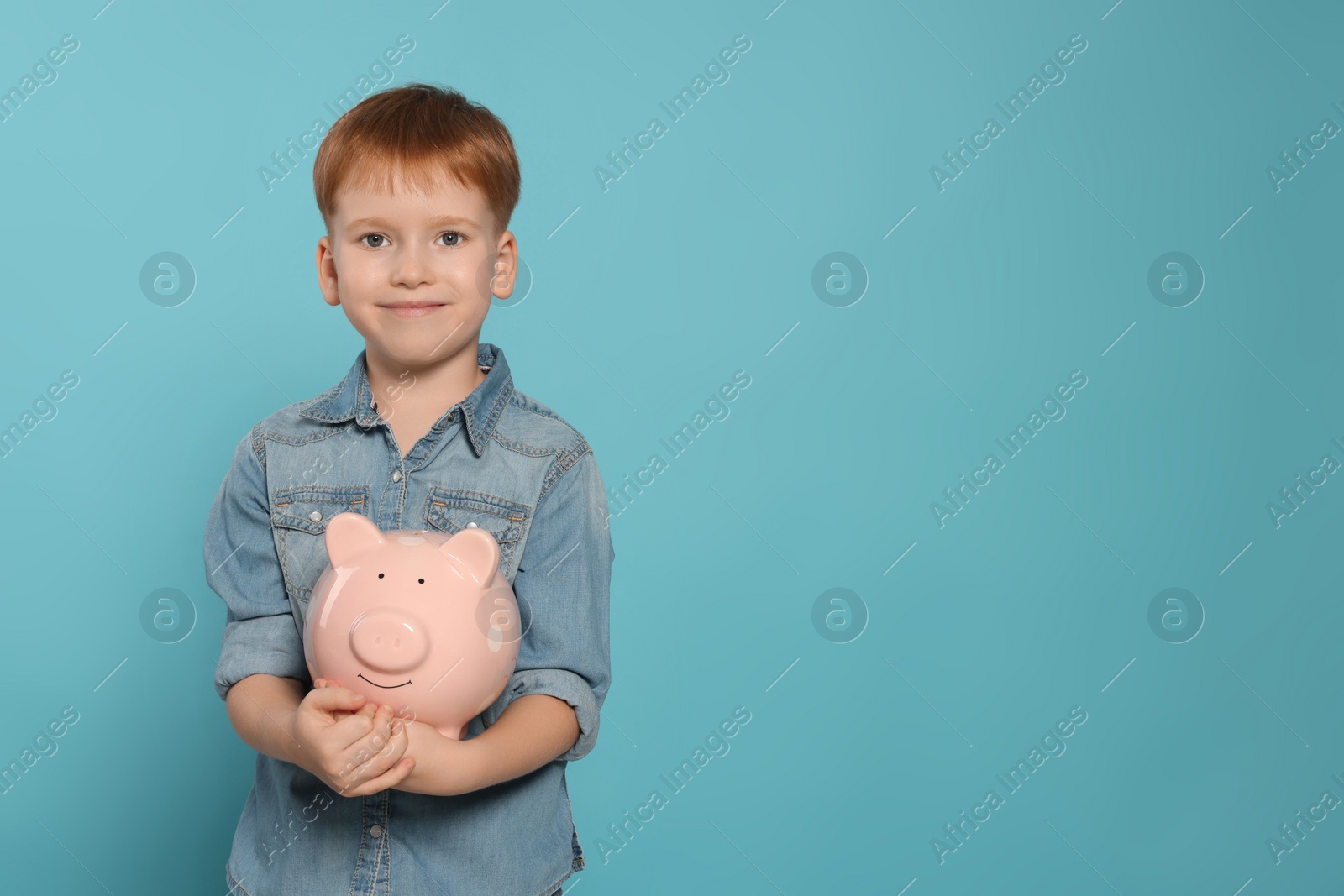 Photo of Cute little boy with ceramic piggy bank on light blue background, space for text