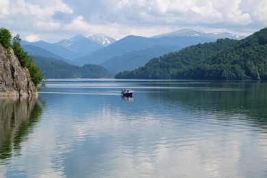 Image of Pleasure boat on lake between hills covered with green forest