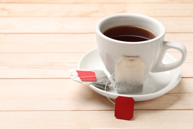 Photo of Tea bags and cup of hot beverage on light wooden table, space for text