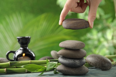 Photo of Woman stacking stones on table against blurred background, closeup. Zen concept