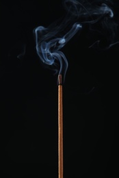 Incense stick smoldering on black background, closeup