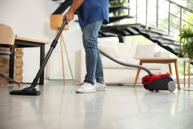Photo of Young man using vacuum cleaner living room, closeup