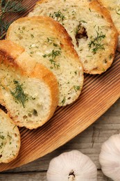 Tasty baguette with garlic and dill on wooden table, top view