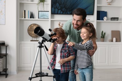 Happy father and children looking at stars through telescope in room