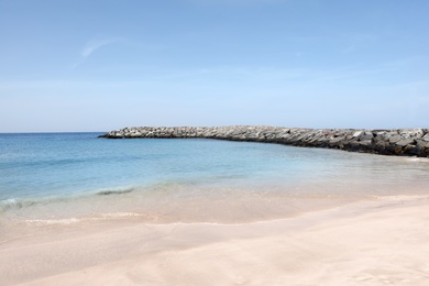 Photo of Picturesque view of beautiful beach with stone breakwater on sunny day