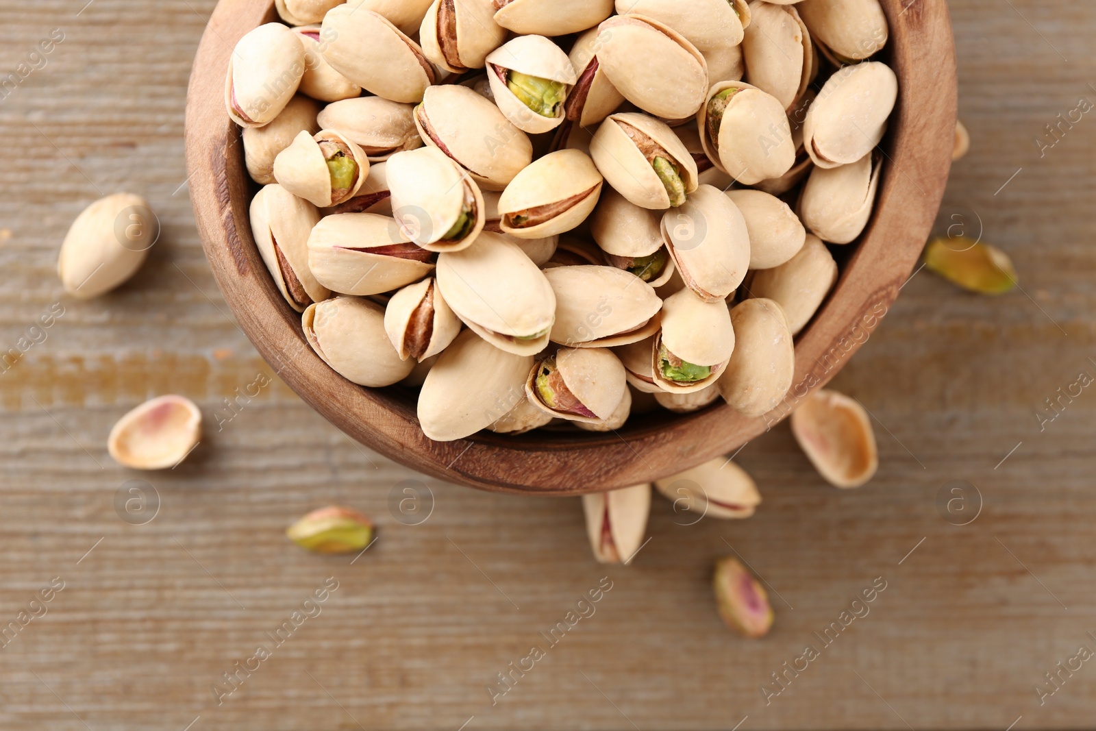 Photo of Tasty pistachios in bowl on wooden table, top view