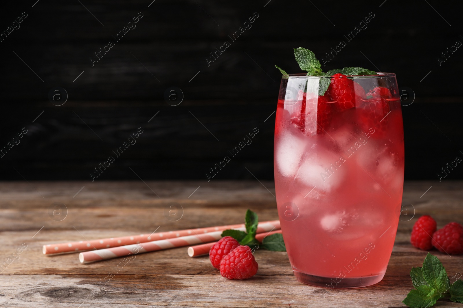 Photo of Glass of refreshing drink with raspberry and mint on wooden table against dark background, space for text