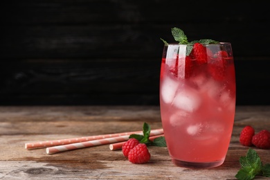 Glass of refreshing drink with raspberry and mint on wooden table against dark background, space for text