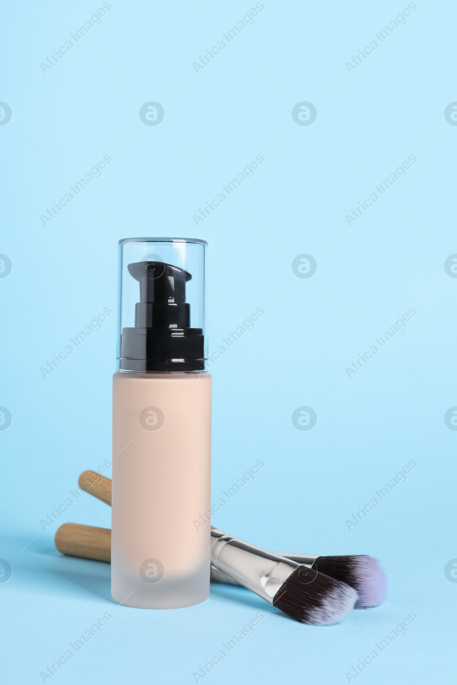 Photo of Bottle of skin foundation and brushes on light blue background. Makeup product