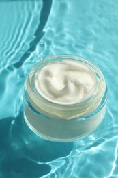 Photo of Jar with moisturizing cream in water on light blue background