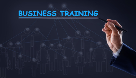 Man pointing at virtual screen with inscription BUSINESS TRAINING on dark background, closeup 