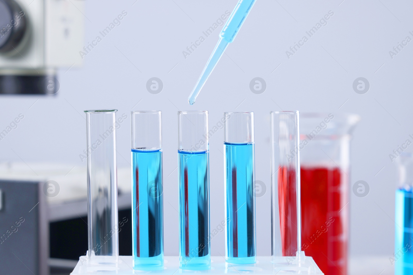 Photo of Dripping liquid from pipette into test tube on blurred background, closeup