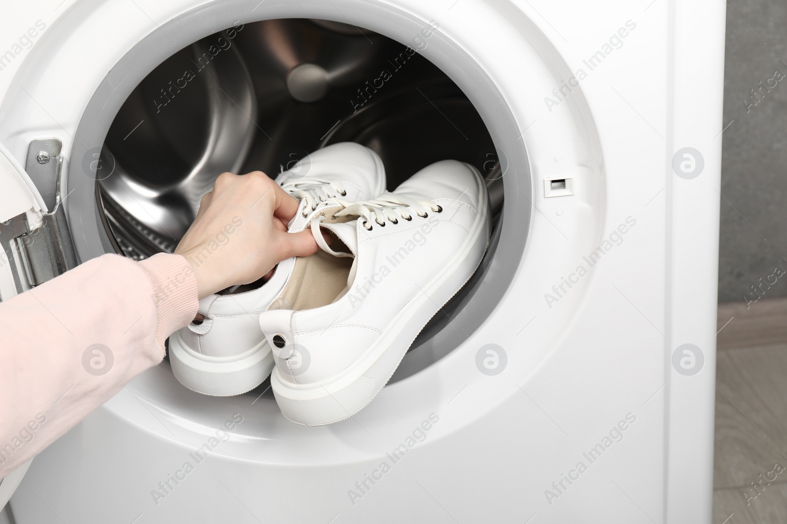 Photo of Woman putting stylish sneakers into washing machine, closeup