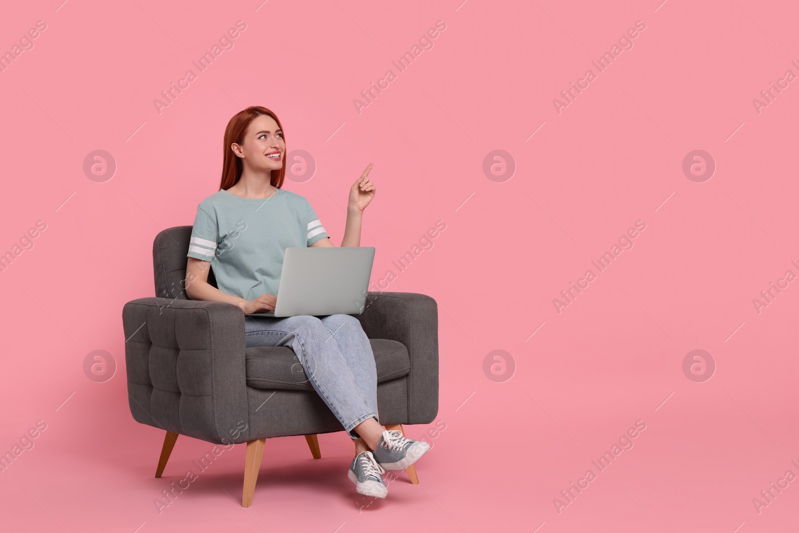 Photo of Smiling young woman with laptop sitting in armchair on pink background, space for text