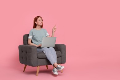 Smiling young woman with laptop sitting in armchair on pink background, space for text