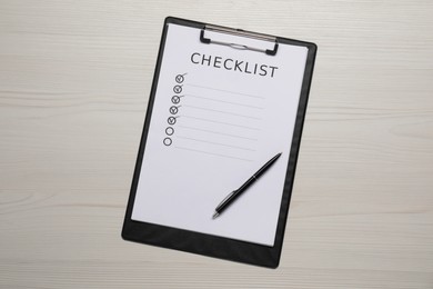 Photo of Clipboard with checklist and pen on wooden table, top view