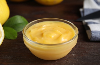 Photo of Delicious lemon curd in bowl on wooden table, closeup