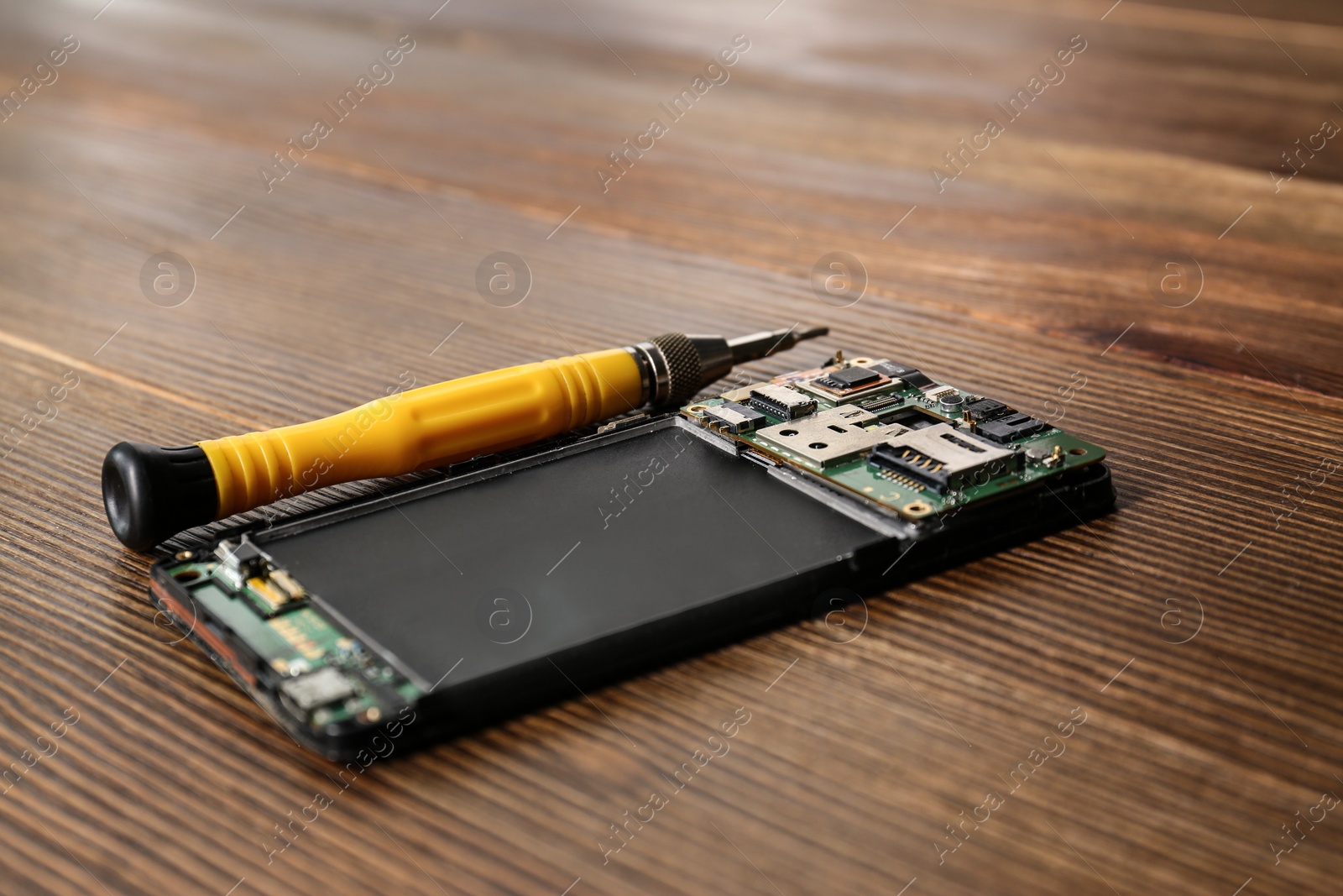 Photo of Broken mobile phone and screwdriver on wooden table, closeup
