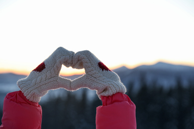 Photo of Woman making heart with her hands in mountains at sunset, closeup. Winter vacation