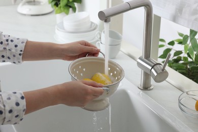 Photo of Woman washing fresh ripe lemons under tap water in kitchen, closeup