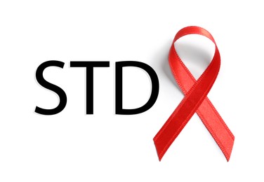 Red awareness ribbon and abbreviation STD on white background, top view 