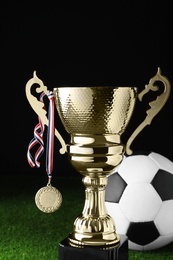 Photo of Golden trophy cup, soccer ball and medal on football field