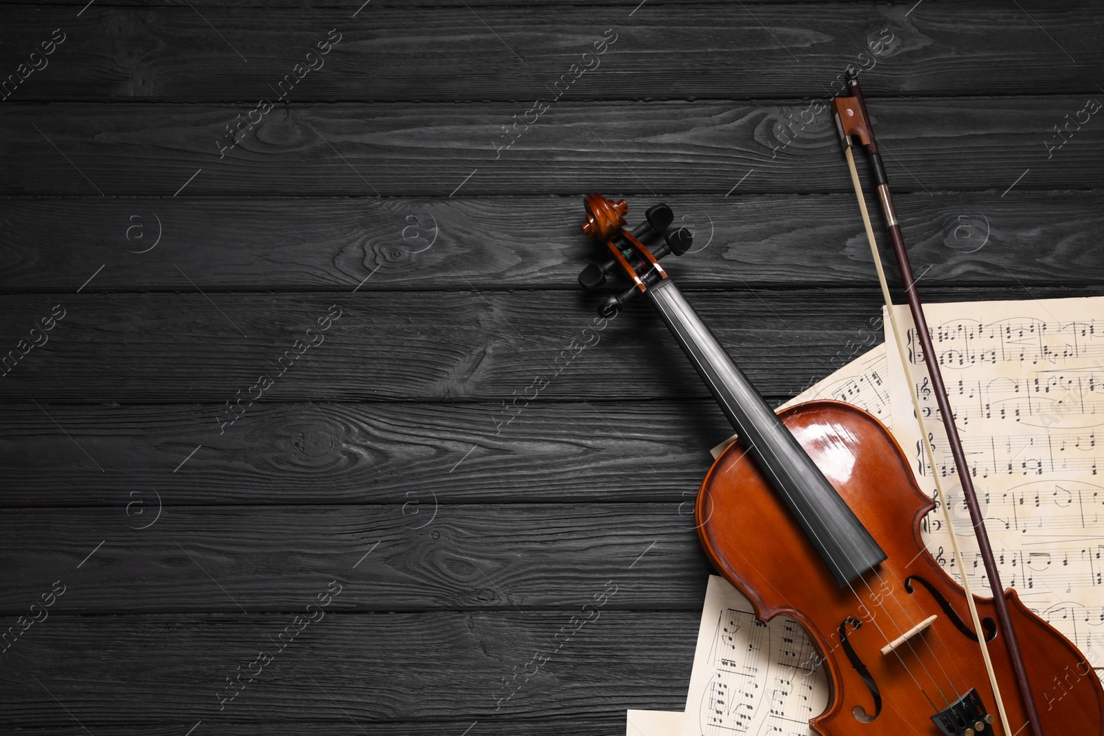 Photo of Violin, bow and music sheets on black wooden table, top view. Space for text